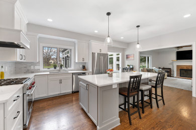Large trendy medium tone wood floor kitchen photo in Milwaukee with a double-bowl sink, white cabinets, gray backsplash, marble backsplash, stainless steel appliances and an island