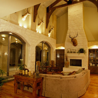 Photo of a large mediterranean formal open plan living room in Austin with beige walls, medium hardwood flooring, a standard fireplace, a stone fireplace surround and brown floors.