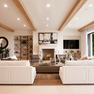 Offenes Mediterranes Wohnzimmer mit weißer Wandfarbe, Kalkstein, Wand-TV, Kamin und beigem Boden in Orange County