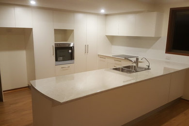 Photo of a mid-sized contemporary u-shaped open plan kitchen in Canberra - Queanbeyan with a drop-in sink, white cabinets, laminate benchtops, white splashback, ceramic splashback, stainless steel appliances, laminate floors, no island, brown floor and beige benchtop.