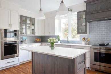 Enclosed kitchen - mid-sized transitional l-shaped medium tone wood floor and brown floor enclosed kitchen idea in Other with an undermount sink, shaker cabinets, white cabinets, quartz countertops, blue backsplash, subway tile backsplash, stainless steel appliances, an island and white countertops