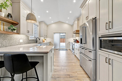 Inspiration for a large classic galley kitchen/diner in Ottawa with a double-bowl sink, shaker cabinets, white cabinets, engineered stone countertops, grey splashback, mosaic tiled splashback, stainless steel appliances, porcelain flooring, a breakfast bar, beige floors, white worktops and a vaulted ceiling.