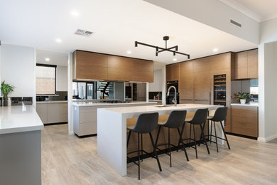 Photo of a large contemporary l-shaped kitchen in Perth with an undermount sink, flat-panel cabinets, medium wood cabinets, mirror splashback, panelled appliances, with island, beige floor and white benchtop.