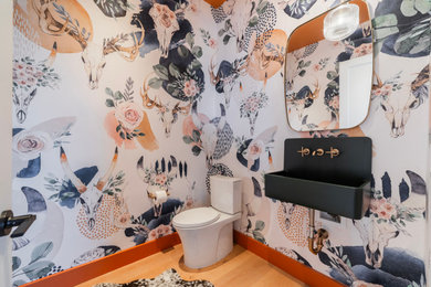 Example of a trendy medium tone wood floor, brown floor and wallpaper powder room design in Austin with multicolored walls and a vessel sink