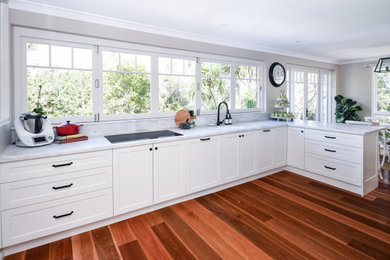 Design ideas for a mid-sized contemporary l-shaped eat-in kitchen in Sydney with a single-bowl sink, shaker cabinets, white cabinets, marble benchtops, marble splashback, black appliances, medium hardwood floors, multiple islands, brown floor and grey benchtop.