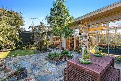 Photo of a mid-sized and australian native midcentury front yard partial sun xeriscape in Melbourne with natural stone pavers.