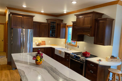 Eat-in kitchen - mid-sized transitional l-shaped light wood floor eat-in kitchen idea in New York with a farmhouse sink, shaker cabinets, brown cabinets, quartz countertops, stainless steel appliances, an island and white countertops
