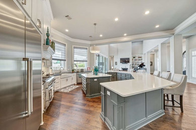 Example of a large transitional u-shaped medium tone wood floor and brown floor open concept kitchen design in Dallas with a farmhouse sink, shaker cabinets, white cabinets, quartz countertops, stainless steel appliances and two islands