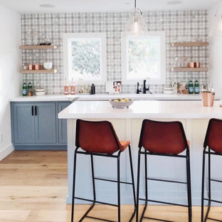 サンフランシスコの大きいビーチスタイルのおしゃれなウェットバー (アンダーカウンターシンク、シェーカースタイル扉のキャビネット、青いキャビネット、珪岩カウンター、マルチカラーのキッチンパネル、ライムストーンの床、淡色無垢フローリング、白いキッチンカウンター) の写真