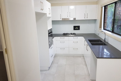 Mid-sized modern u-shaped eat-in kitchen in Sydney with a double-bowl sink, flat-panel cabinets, white cabinets, quartz benchtops, white splashback, glass sheet splashback, stainless steel appliances, porcelain floors, no island, white floor and grey benchtop.