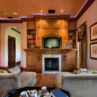 Kleines, Abgetrenntes Mediterranes Wohnzimmer mit rosa Wandfarbe, braunem Holzboden, Tunnelkamin, Kaminsims aus Stein und Multimediawand in Orlando