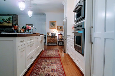 Inspiration for a mid-sized cottage galley medium tone wood floor and brown floor open concept kitchen remodel in Montreal with a farmhouse sink, shaker cabinets, white cabinets, wood countertops, white backsplash, subway tile backsplash, stainless steel appliances, an island and brown countertops
