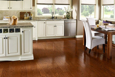 Example of a transitional l-shaped medium tone wood floor and brown floor eat-in kitchen design in Seattle with an undermount sink, raised-panel cabinets, white cabinets, granite countertops, beige backsplash, porcelain backsplash, stainless steel appliances and an island