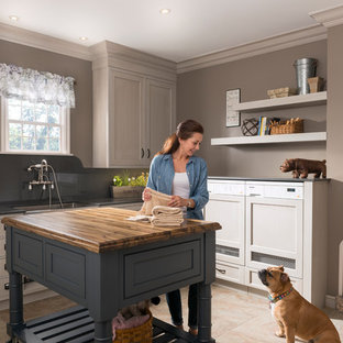Photo of a large classic l-shaped utility room in Other with a belfast sink, recessed-panel cabinets, white cabinets, porcelain flooring, a concealed washer and dryer and grey walls.