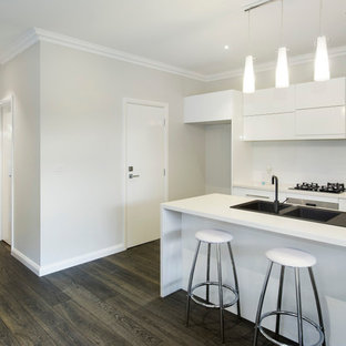 Mid-sized contemporary kitchen pantry pictures - Inspiration for a mid-sized contemporary single-wall dark wood floor kitchen pantry remodel in Melbourne with an integrated sink, recessed-panel cabinets, white cabinets, granite countertops, white backsplash, ceramic backsplash, stainless steel appliances and an island