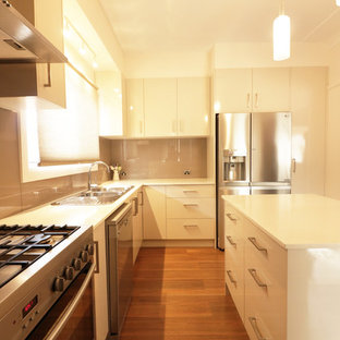 Пример оригинального дизайна: п-образная кухня среднего размера в современном стиле с кладовкой, накладной раковиной, плоскими фасадами, бежевыми фасадами, столешницей из кварцевого композита, коричневым фартуком, фартуком из стекла, техникой из нержавеющей стали, светлым паркетным полом, островом и желтым полом