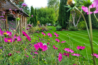Large country back formal and private fully shaded garden for spring in Kent with decking and a wood fence.
