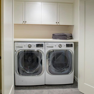 Diseño de armario lavadero lineal, de estilo americano, pequeño, con armarios estilo shaker, puertas de armario blancas, encimera de madera, suelo de cemento, lavadora y secadora juntas y paredes beige