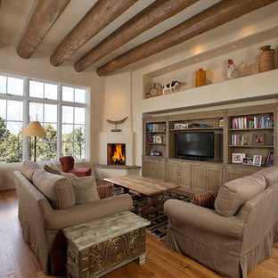 Offene, Mittelgroße Mediterrane Bibliothek mit beiger Wandfarbe, braunem Holzboden, Eckkamin, freistehendem TV und verputztem Kaminsims in Albuquerque