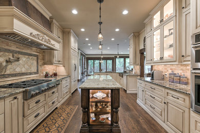 Huge elegant galley dark wood floor and brown floor enclosed kitchen photo in Oklahoma City with a farmhouse sink, raised-panel cabinets, light wood cabinets, granite countertops, brown backsplash, travertine backsplash, stainless steel appliances and an island