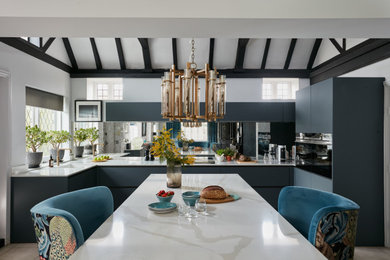 Medium sized modern grey and white u-shaped kitchen/diner in London with flat-panel cabinets, grey cabinets, composite countertops, mirror splashback, black appliances, an island, white worktops, a built-in sink, exposed beams and feature lighting.