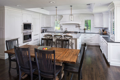 Eat-in kitchen - large traditional u-shaped dark wood floor eat-in kitchen idea in New York with a farmhouse sink, beaded inset cabinets, white cabinets, quartzite countertops, gray backsplash, subway tile backsplash, paneled appliances and an island