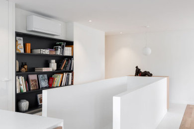 Cette photo montre une salle de séjour tendance de taille moyenne et ouverte avec une bibliothèque ou un coin lecture, un mur blanc, parquet clair et un téléviseur fixé au mur.