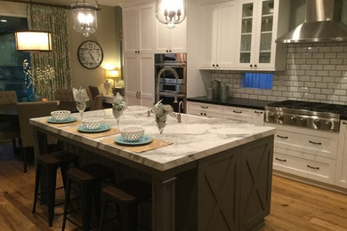 Inspiration for a mid-sized transitional l-shaped medium tone wood floor and brown floor eat-in kitchen remodel in San Diego with a farmhouse sink, shaker cabinets, white cabinets, solid surface countertops, white backsplash, subway tile backsplash, stainless steel appliances and an island