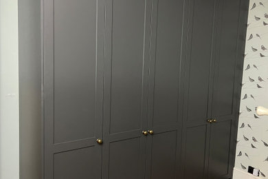 Design ideas for a medium sized traditional built-in wardrobe for men in London with shaker cabinets, grey cabinets, light hardwood flooring and feature lighting.