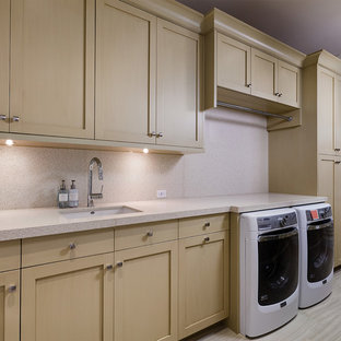 他の地域の大きいトラディショナルスタイルのおしゃれな洗濯室 (アンダーカウンターシンク、落し込みパネル扉のキャビネット、淡色木目調キャビネット、再生ガラスカウンター、ベージュの壁、セラミックタイルの床、左右配置の洗濯機・乾燥機、ベージュの床、ベージュのキッチンカウンター) の写真
