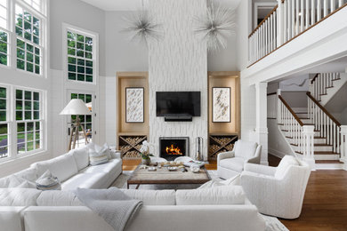 Photo of a large transitional formal open concept living room in New York with white walls, medium hardwood floors, a standard fireplace, a wall-mounted tv and brown floor.
