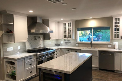 Photo of a kitchen in San Francisco with a farmhouse sink, shaker cabinets, white cabinets, stainless steel appliances, with island and brown floor.