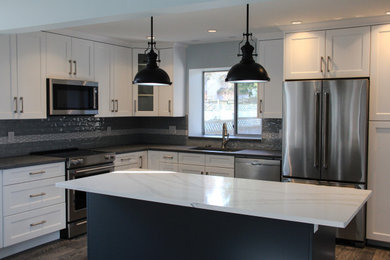 Example of a large trendy l-shaped laminate floor and multicolored floor open concept kitchen design in Vancouver with an undermount sink, shaker cabinets, white cabinets, quartz countertops, gray backsplash, subway tile backsplash, stainless steel appliances, an island and white countertops