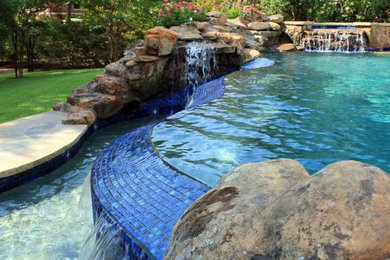 Inspiration for a mid-sized contemporary backyard custom-shaped infinity pool in Austin with a water feature and natural stone pavers.