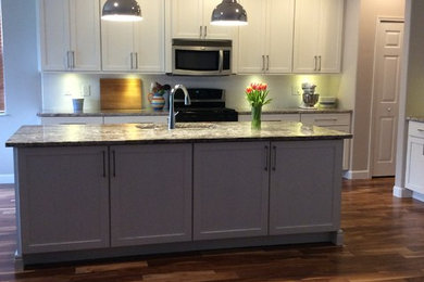 Mid-sized transitional l-shaped medium tone wood floor and brown floor eat-in kitchen photo in Orlando with an undermount sink, shaker cabinets, white cabinets, granite countertops, white backsplash, ceramic backsplash, stainless steel appliances and an island