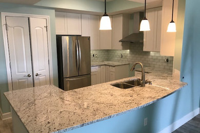 Mid-sized beach style u-shaped eat-in kitchen photo in Jacksonville with a double-bowl sink, shaker cabinets, white cabinets, granite countertops, white backsplash, subway tile backsplash, stainless steel appliances, a peninsula and brown countertops