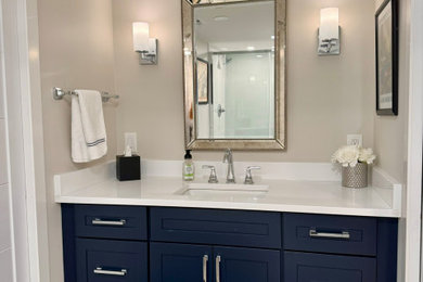 Inspiration for a medium sized classic shower room bathroom in Detroit with shaker cabinets, blue cabinets, an alcove shower, a two-piece toilet, white tiles, marble tiles, beige walls, porcelain flooring, a submerged sink, engineered stone worktops, black floors, a sliding door, white worktops, a single sink and a built in vanity unit.