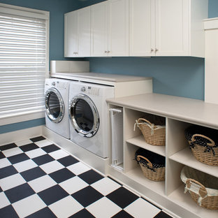 チャールストンの大きいトラディショナルスタイルのおしゃれな洗濯室 (落し込みパネル扉のキャビネット、白いキャビネット、ラミネートカウンター、青い壁、クッションフロア、左右配置の洗濯機・乾燥機) の写真