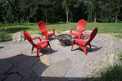 This is an example of a mid-sized country side yard patio in New York with natural stone pavers, a fire feature and no cover.