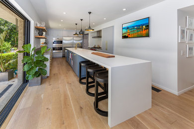 Inspiration for a large transitional galley separate kitchen in Los Angeles with an integrated sink, flat-panel cabinets, grey cabinets, quartz benchtops, stainless steel appliances, light hardwood floors and with island.