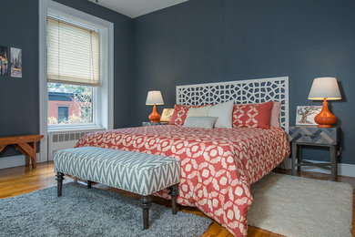 Example of a mid-sized transitional master medium tone wood floor and brown floor bedroom design in New York with gray walls, a standard fireplace and a stone fireplace