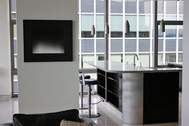 Inspiration for a large modern l-shaped limestone floor and beige floor open concept kitchen remodel in Austin with an island, an undermount sink, flat-panel cabinets, black cabinets, solid surface countertops, limestone backsplash and stainless steel appliances