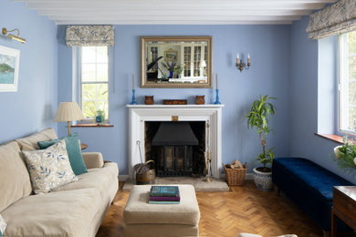 Ejemplo de salón con rincón musical cerrado clásico pequeño con paredes azules, suelo de madera en tonos medios, estufa de leña, marco de chimenea de madera, suelo marrón, vigas vistas y cortinas