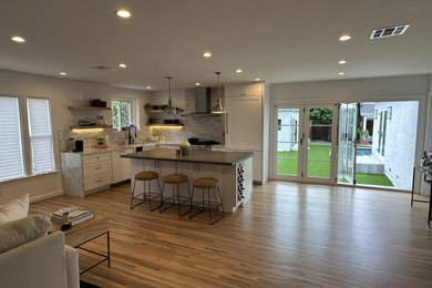 Inspiration for a large transitional l-shaped medium tone wood floor and brown floor eat-in kitchen remodel in Los Angeles with a farmhouse sink, shaker cabinets, white cabinets, marble countertops, gray backsplash, subway tile backsplash, paneled appliances, an island and gray countertops