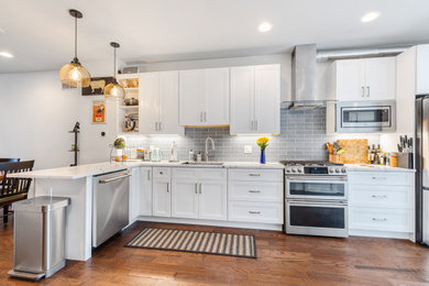 Inspiration for a mid-sized contemporary l-shaped medium tone wood floor eat-in kitchen remodel in Philadelphia with an undermount sink, shaker cabinets, white cabinets, quartz countertops, blue backsplash, porcelain backsplash, stainless steel appliances, a peninsula and white countertops