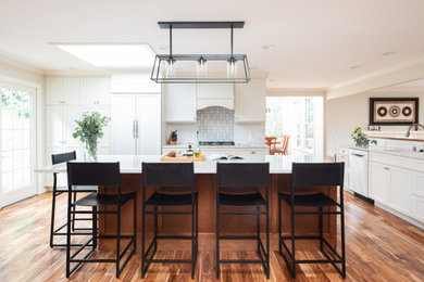 Elegant medium tone wood floor and brown floor kitchen photo in Seattle with an undermount sink, shaker cabinets, white cabinets, white backsplash, subway tile backsplash, stainless steel appliances, an island and white countertops