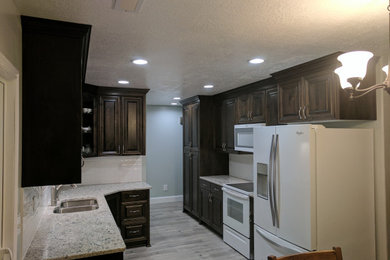 Mid-sized trendy galley laminate floor and gray floor eat-in kitchen photo in Salt Lake City with an undermount sink, raised-panel cabinets, dark wood cabinets, granite countertops, white backsplash, subway tile backsplash, white appliances, no island and beige countertops