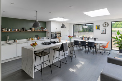 Mid-sized modern l-shaped eat-in kitchen in Sussex with an undermount sink, flat-panel cabinets, white cabinets, quartzite benchtops, green splashback, stainless steel appliances, dark hardwood floors, with island, grey floor and white benchtop.