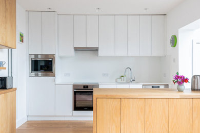 Design ideas for a medium sized contemporary open plan kitchen in Devon with flat-panel cabinets, white cabinets, wood worktops, white splashback, integrated appliances and an island.