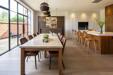 This is an example of a large midcentury l-shaped eat-in kitchen in London with an integrated sink, flat-panel cabinets, medium wood cabinets, quartzite benchtops, white splashback, stone slab splashback, stainless steel appliances, medium hardwood floors, with island, brown floor and white benchtop.